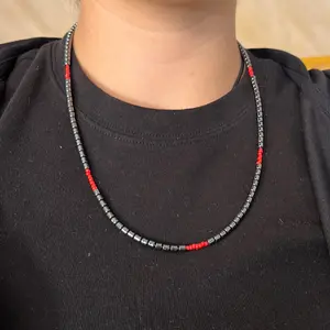 An authentic Navajo handmade necklace featuring hematite, red coral, liquid silver beads, and silver daisy shaped beads.