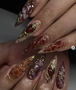 Luxury stiletto nails with deep red marble effect, glossy finish, and gold metallic accents, creating a bold, artistic, and gemstone-inspired look