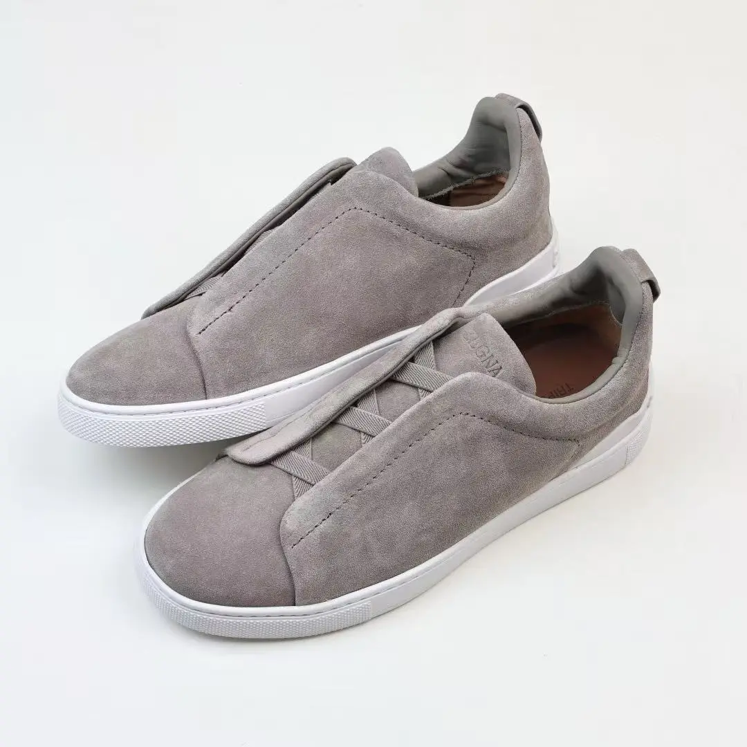 Light Gray Suede Slip-On No Lace Low Top Casual Skate Shoes Soft Full Grain Nubuck Upper Hidden Crisscross Webbing Strap Minimal Straight Stitch Seams Clean White Textured Rubber Flat Outsole Unisex Business Minimalist Daily Walking Trainers