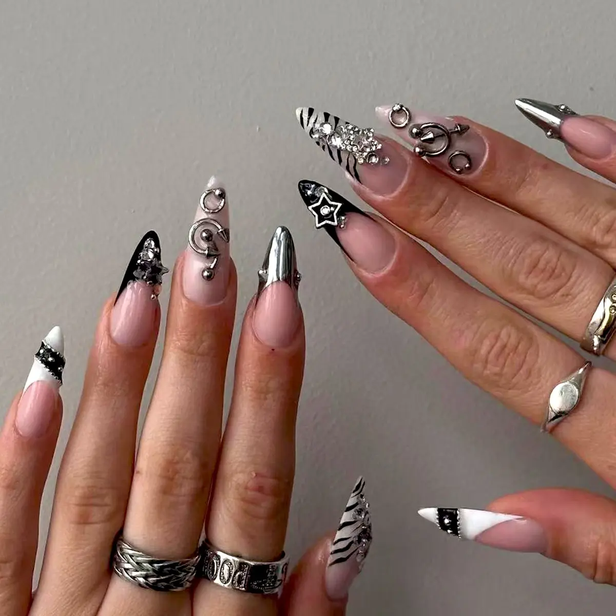 24pcs Long pointed press on nails in a punk/edgy style, Crazy nail art, featuring 3D nose ring and hoop designs, metallic black and white gradient zebra stripes, white rhinestones, and silver French tip nails