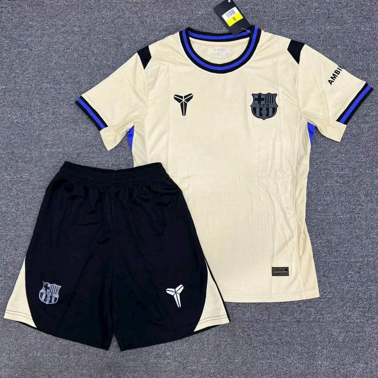 Barcelona Mamba Soccer Jersey Set Grey Carpet Flat Lay Display | Cream Black Short Sleeve Kit Shorts | UEFA Champions League Fan Gear Apparel Gift