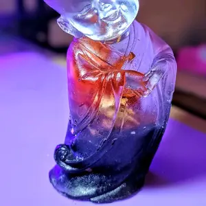 Adorable baby monk statue with heart hands, featuring an encased orange Lily.
