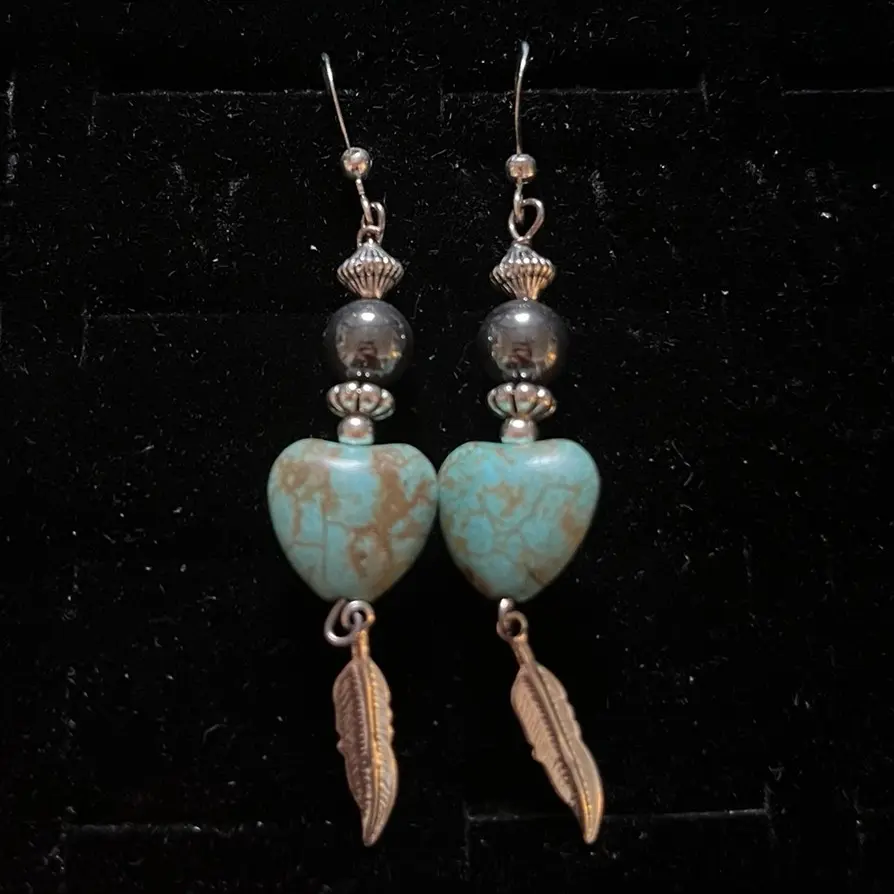 These Navajo handmade sterling silver hook earrings featuring globe Turquoise, hematite, silver daisy-shaped bead, silver hogan bead And silver plated feathers.