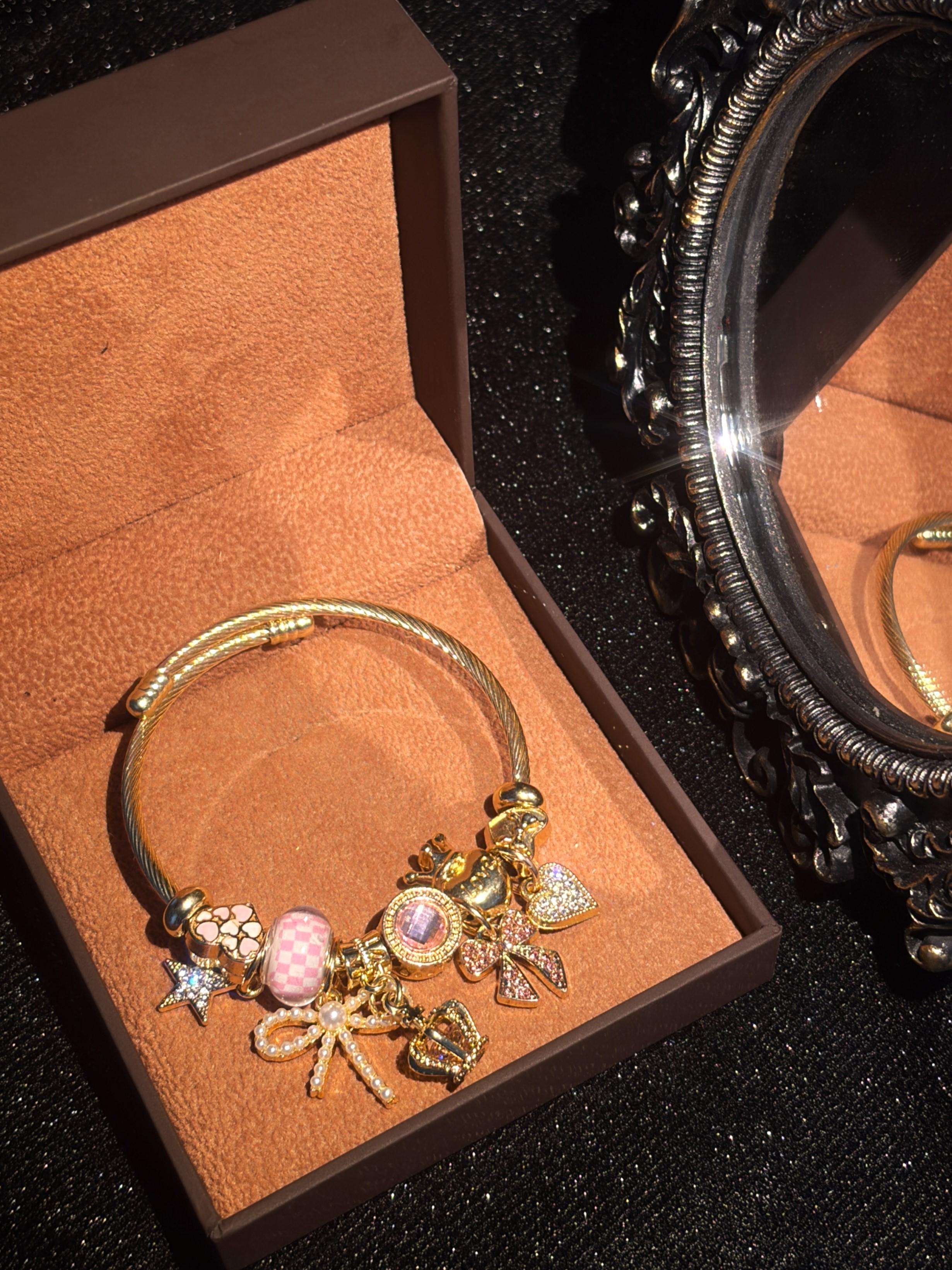 Women's Cute Princess-Style Gold-Tone Adjustable Cable Bangle with Pink Checkered Bead, Bow, Crown, and Heart Dangle Charms Women's Cute Princess-Style Gold-Tone Adjustable Cable Bangle with Pink Checkered Bead, Bow, Crown, and Heart Dangle Charms