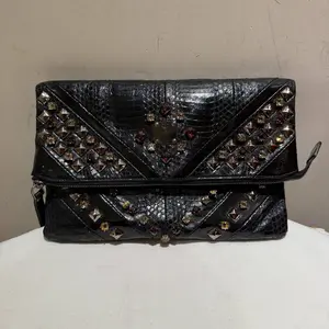 Pre-owned MCM leather Clutches & Wristlets black clutch features a reptile embossed exterior and is adorned with dark toned studded pyramid hardware