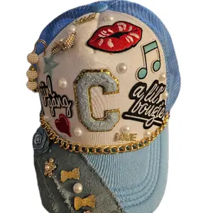 This one-of-a-kind trucker hat is the perfect blend of bold, fun, and fashionable! Featuring a soft baby blue mesh and denim base, the front is decked out with eye-catching embellishments including embroidered red lips, glittering gold accents and pearls.