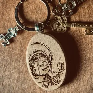 Granny’s Wisdom Charm Keychain. Wood engraved with a portrait of Granny Goblin. Completed with a mini Frogmire charm.