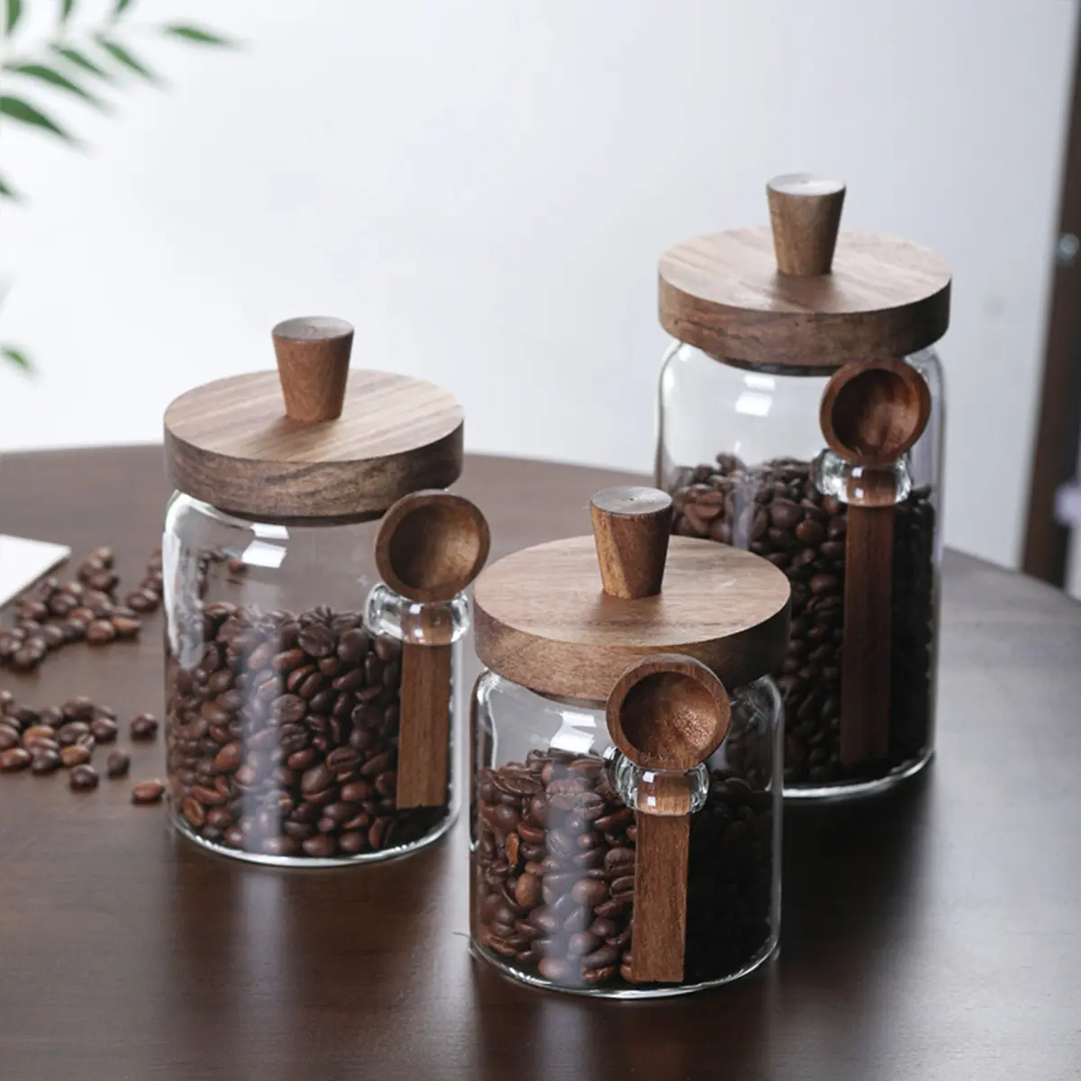 A set of 3 glass coffee bean storage containers with wooden lids and spoons, which aids in organizing the kitchen while also enhancing its aesthetic appeal.