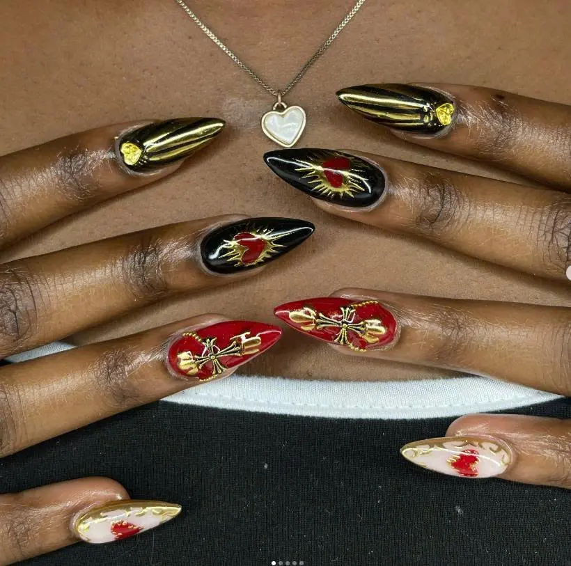A striking set of pointed nails featuring bold red and black hues with gold accents, showcasing heart and bow designs for a glamorous yet edgy style.