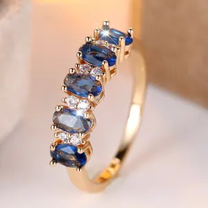 A gold egg-shaped ring with a sapphire blue edge and white diamonds, made of synthetic blue zirconia, is suitable for women to wear daily at wedding parties