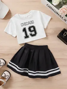 Sweet And Elegant Little Girl With Digital Letter Print T-shirt And Contrasting Striped Pleated Skirt Suitable For Casual Vacation Parties