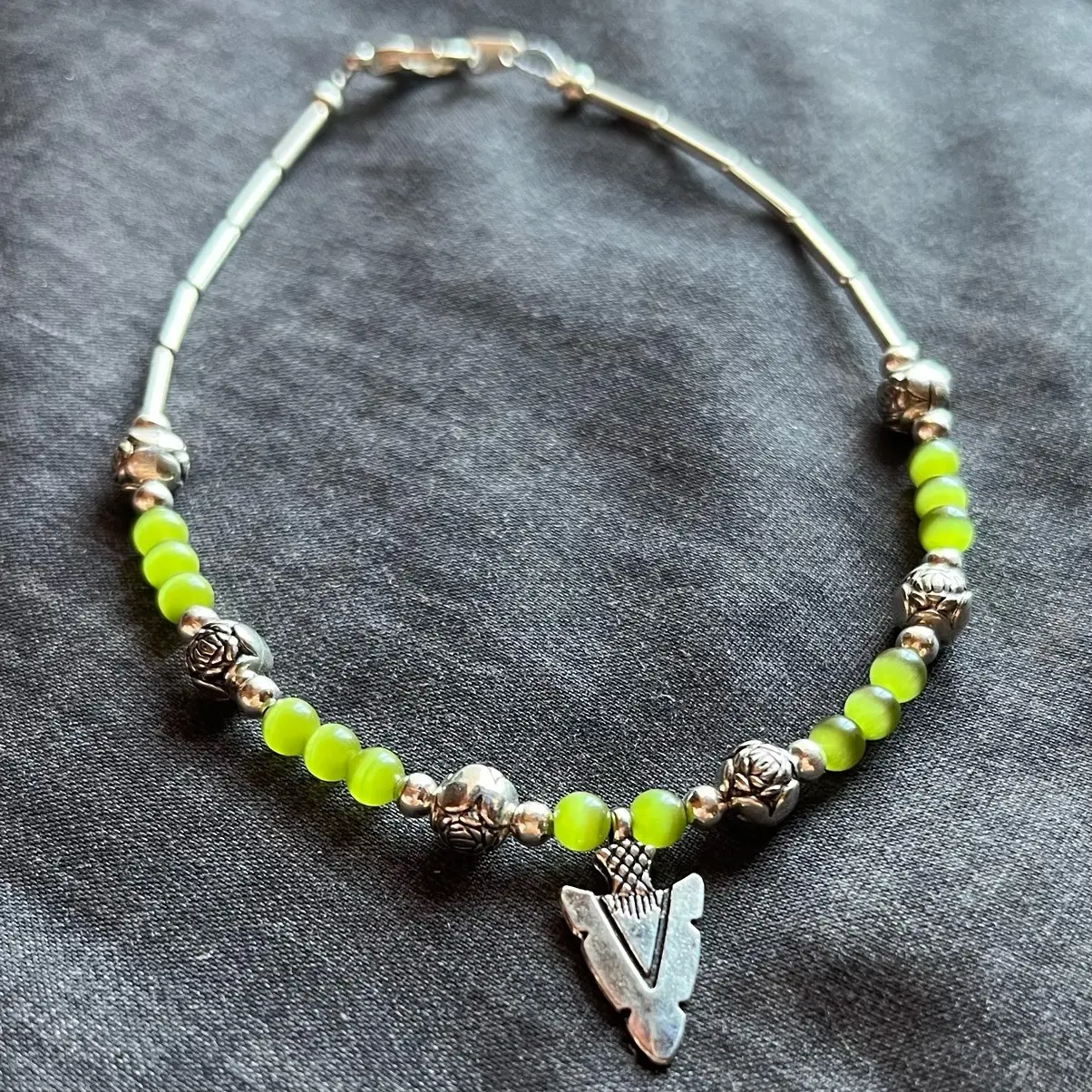 A handcrafted silver arrowhead charm anklet featuring green jade stones and silverplated rosebud bead design indigenous to the Navajo people.