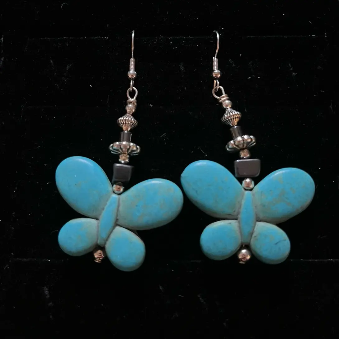 Navajo handmade sterling silver earrings adorned with a magnesite turquoise butterfly bead, hematite, silver daisy-shaped bead and silver hogan bead.