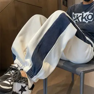 A pair of apricot-colored corduroy jogger pants with navy side stripes, street style fashion, featuring a drawstring waistband for a casual street vibe. The side navy stripe design adds a trendy personal touch, making it easily recognizable in streetwear.