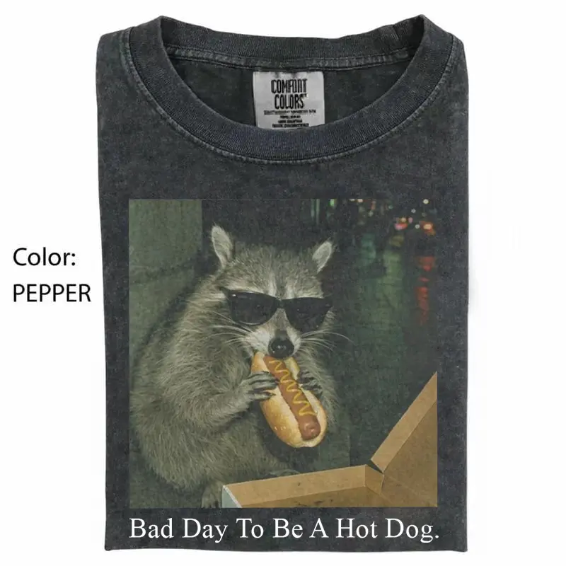 Bad Day To Be A Hot Dog. Comfort Colors Raccoon Eating Hot Dog T-Shirt featuring a funny meme graphic, silly animal humor design, vintage retro unisex cotton top and cute gift for men and women alike.