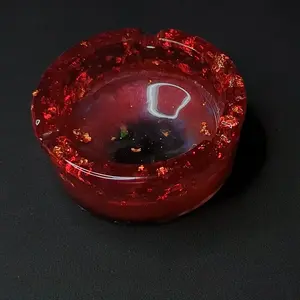 Hand-crafted iridescent red and gold resin ashtray. Not just a feast for the eyes, our ashtray is also practical, with smooth edges and a deep bowl to hold your ashes securely. Its minimalist and sparkly design complements any decor.
