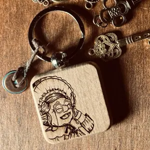 Granny’s Luck Charm Keychain. Wood engraved with a portrait of Granny Goblin. Completed with a lucky button