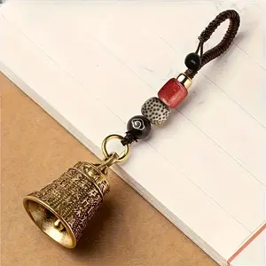 Handmade Tibetan bell keychain, featuring woven rope and beads - intricate carved design, red and black beads, gold cover, Buddhist mantra bell, for good luck, travel, camping, and as a holiday gift, travel accessory |   Artistic Pendant |   Beaded decora
