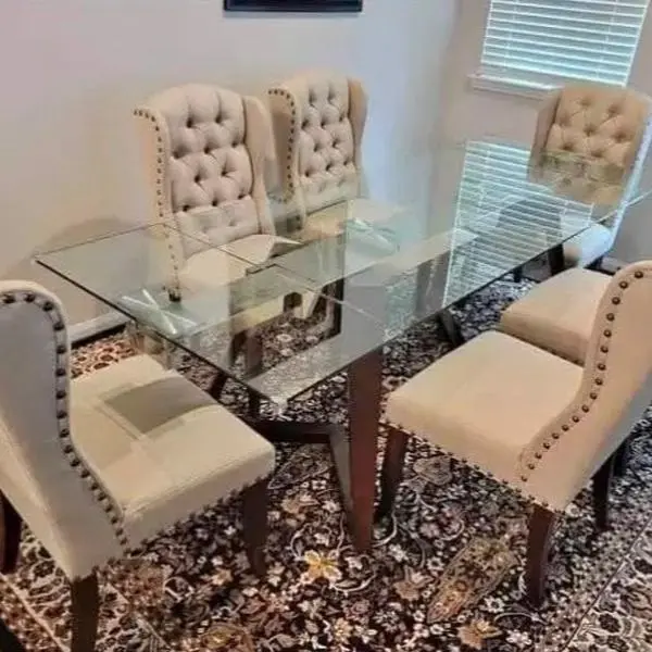 Modern dining set features a glass table with a wooded base and beige tufted chairs.