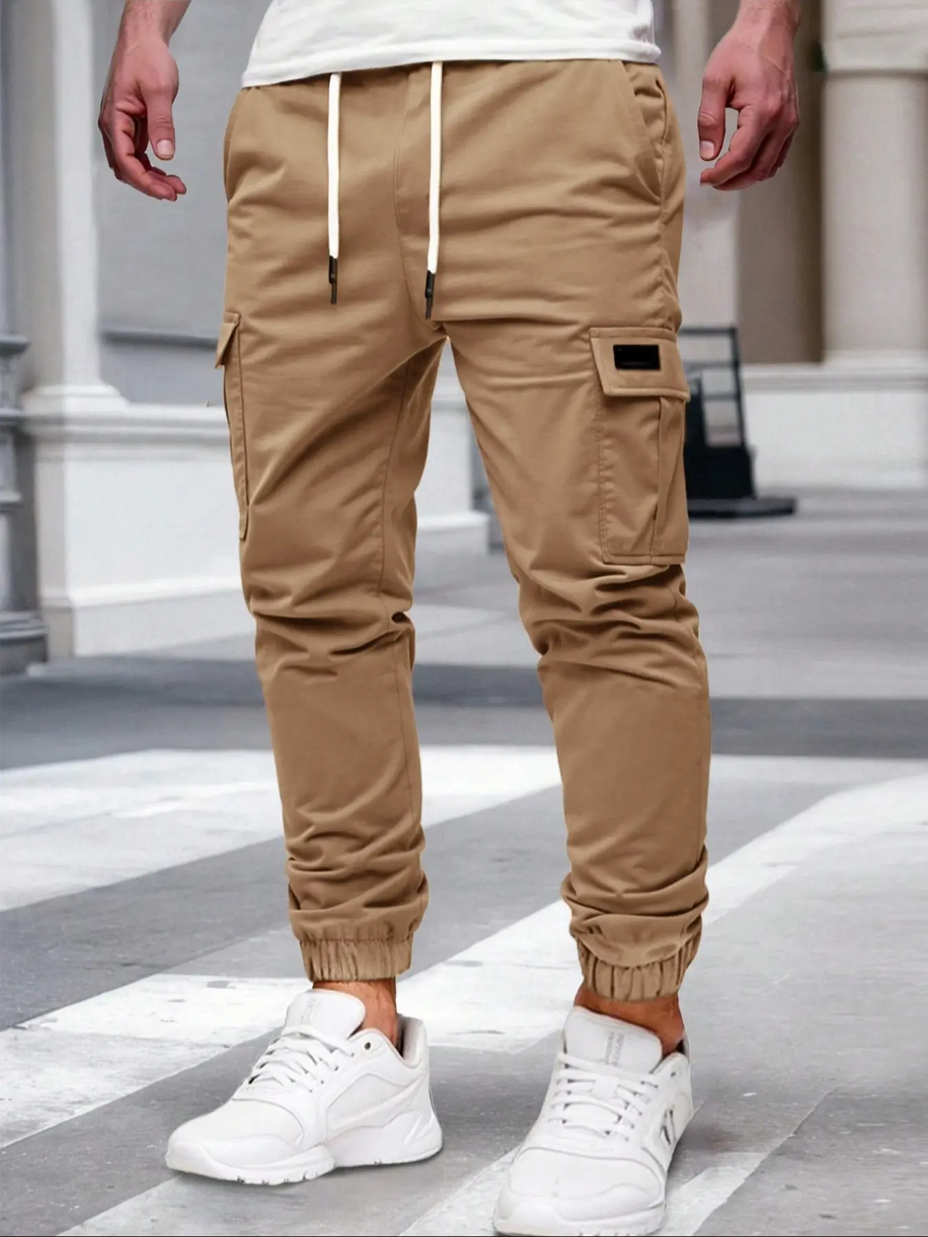 Men's solid - color cargo joggers have an adjustable waist drawstring. These men's cargo long pants feature multiple pockets on both sides, and the pockets are designed with square patches. They are also men's casual cargo style long pants.