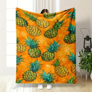 This blanket is covered with hand-painted pineapples, with yellow-green flesh and turquoise leaves, set against a warm orange background that brings a vivid tropical vibe. It is soft and skin-fri
