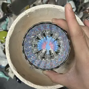 A masterpiece, a silver-glazed teacup with a hand-painted peacock design, luminous.