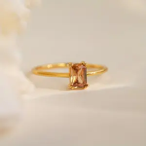 A minimalist, luxury-inspired solitaire ring featuring a champagne-colored synthetic zirconia in an emerald cut, set with a classic four-prong setting. This elegant, niche design complements a variety of styles and makes for a stunning wedding ring.