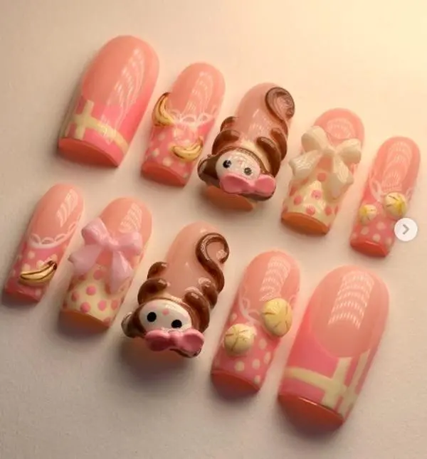 kawaii press on nails with pastel pink base, 3d monkey face, bananas, bows and polka dots for a playful cute cartoon inspired nail art look