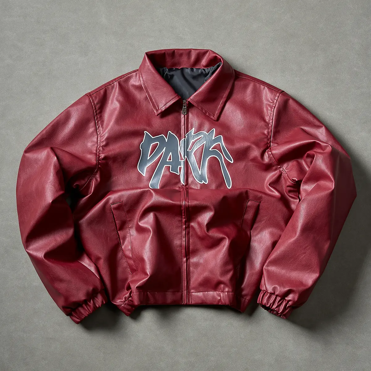 One men’s black faux leather short jacket with a turn-down collar and letter print; American retro casual style with sharp, irregular graffiti lines and a dynamic feel; symmetrical side pockets that balance practicality and aesthetics; relaxed short fit w