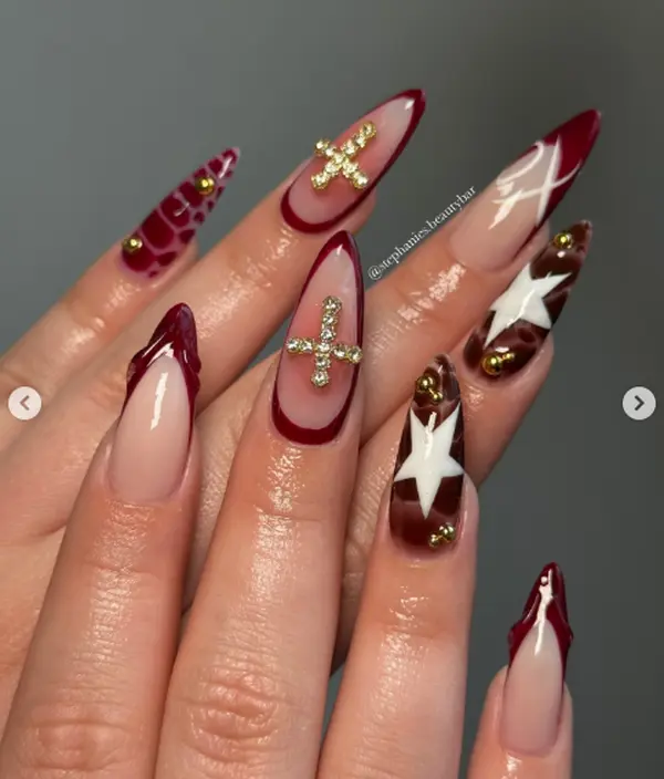 Burgundy French tip stiletto nails with gold cross charms, white stars and tortoise accents for a luxe coquette gothic look