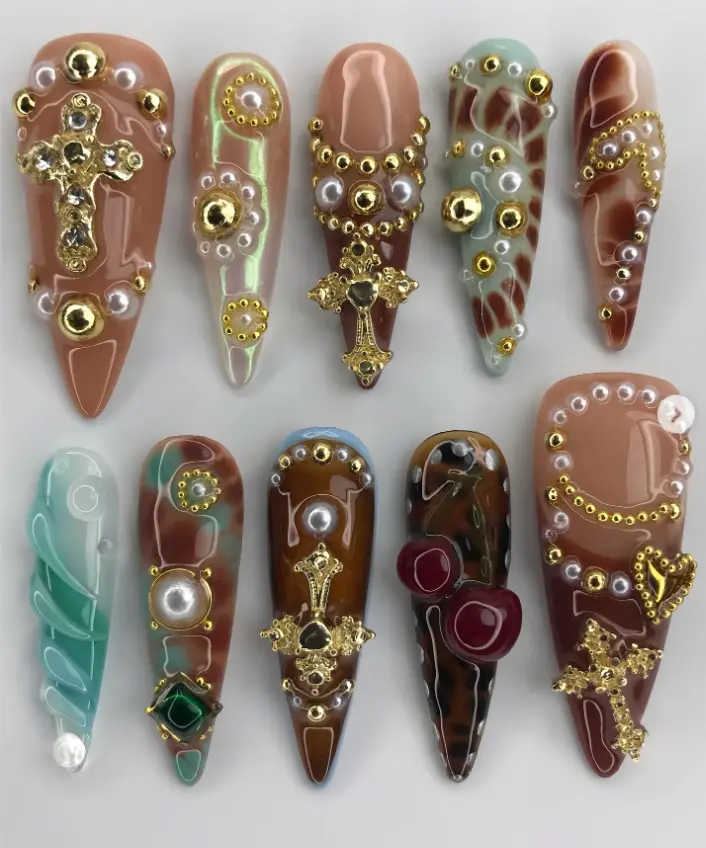 Luxurious nail art with rich earthy tones, gold crosses, pearls, and intricate 3D details, perfect for a bold, regal, and high-fashion statement look