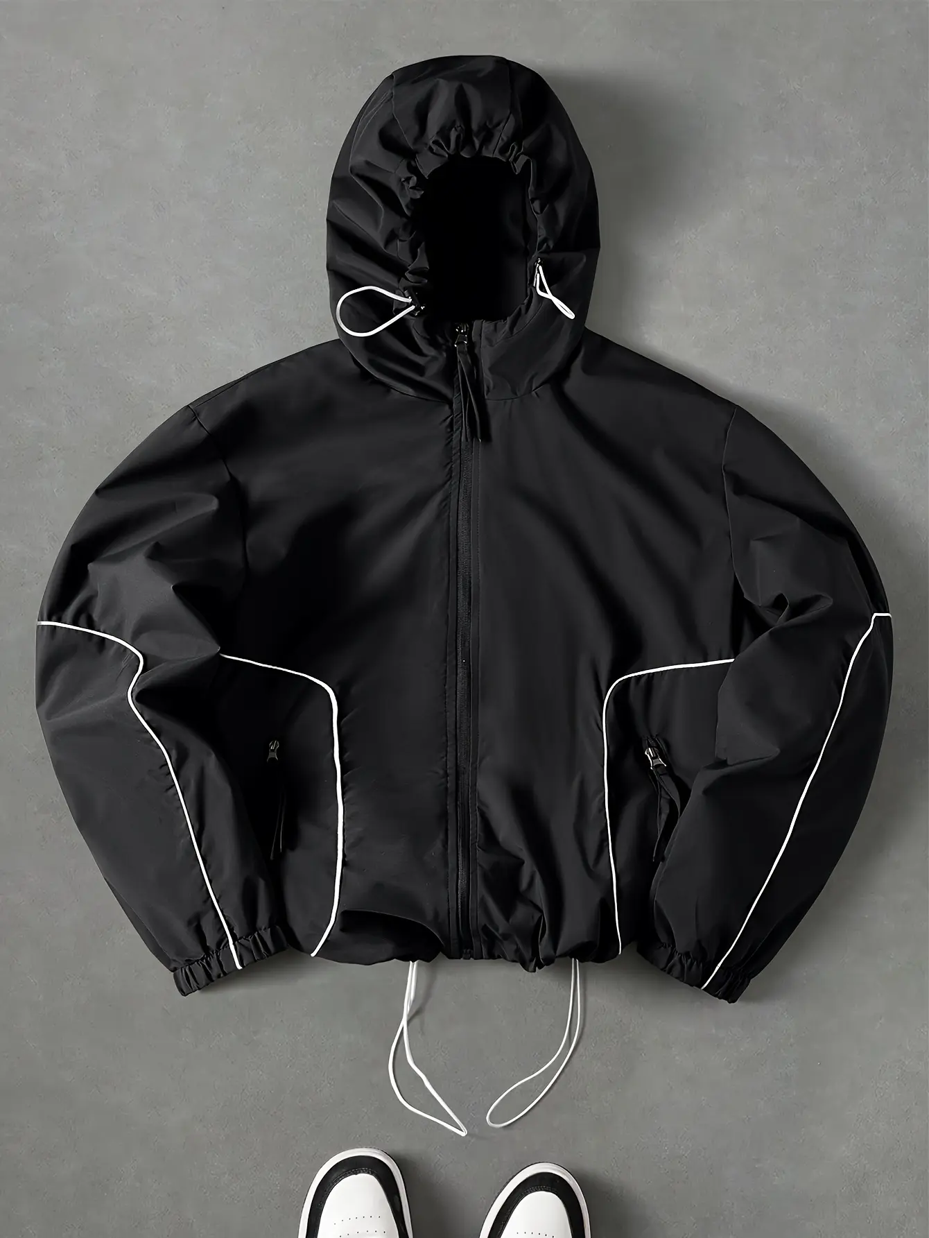 Men’s black varsity-style hooded jacket with white contrast piping, hat + double drawstring hem design, side zipper pockets, loose short length, trendy street-style windbreaker with a sporty feel.