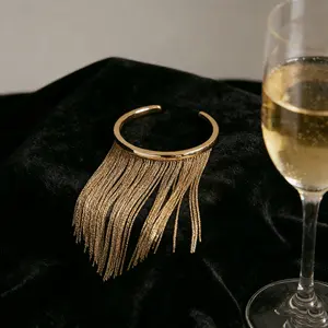The "Gilded Tassel" open bangle combines fluid tassel chains with a polished metal band, serving as the quintessential accessory for cultivating an atmospheric aura and a sense of lively elegance.