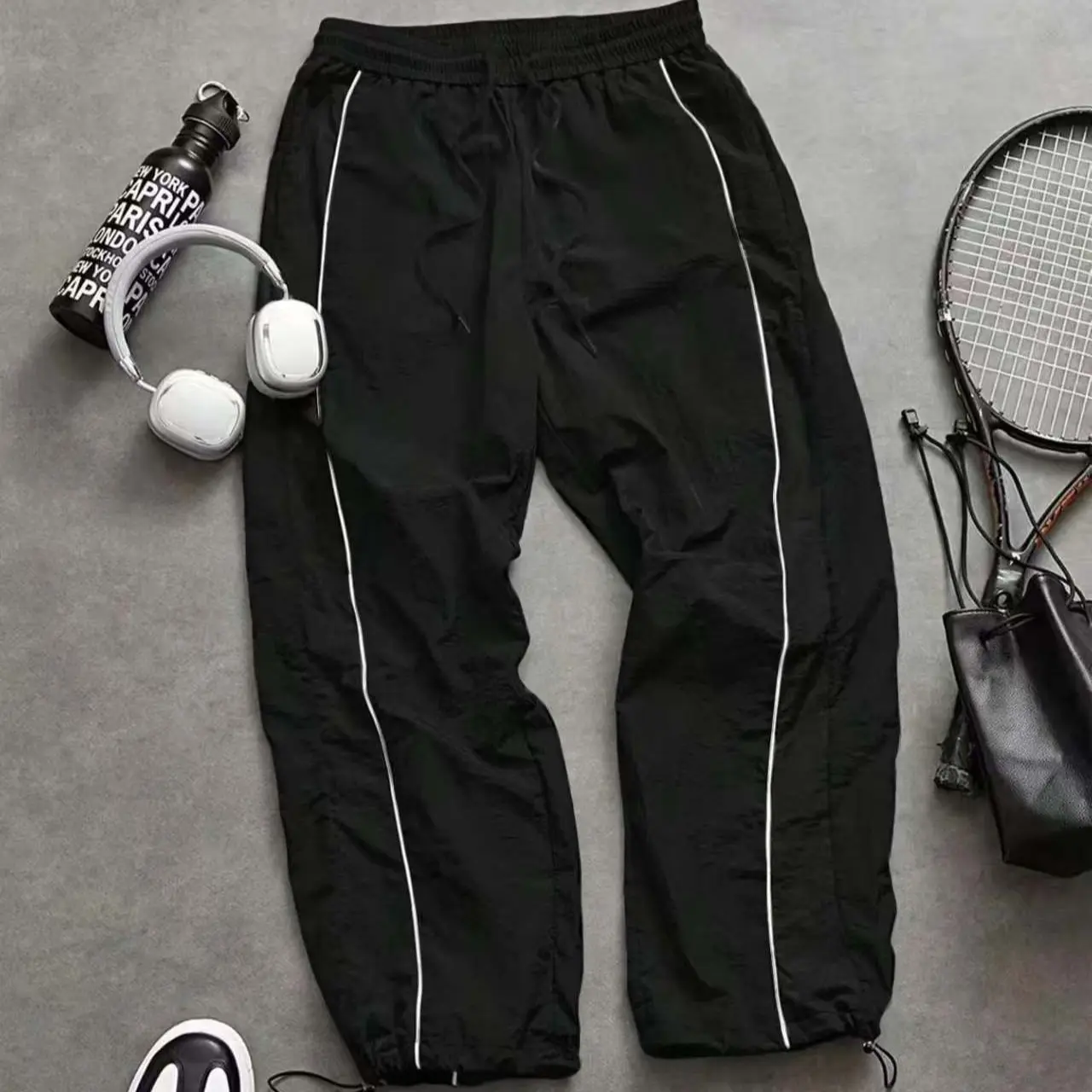 Men’s casual parachute pants with white side stripe detailing, elastic drawstring waist, adjustable drawcords at the pant legs, wide parachute-style cut, Y2K retro sporty street-casual style, loose and comfortable for everyday wear.